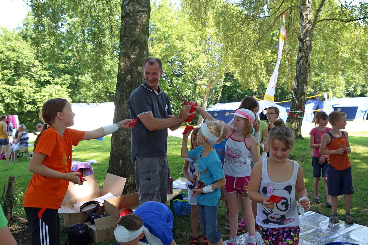 Ein ASJ-Mitarbeiter steht umringt von einem halben Dutzend Kinder in einem Ferienlager.